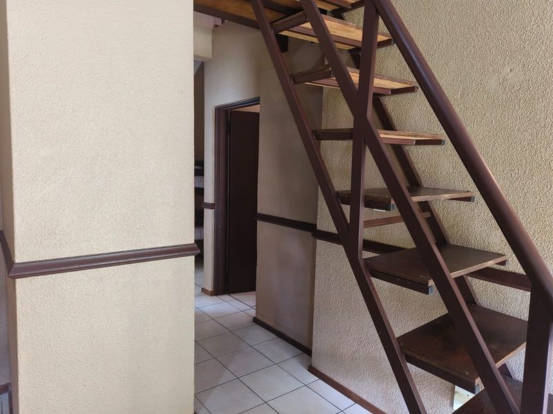 A hallway featuring a metal staircase with wooden treads and tiled flooring, leading to an adjacent room.