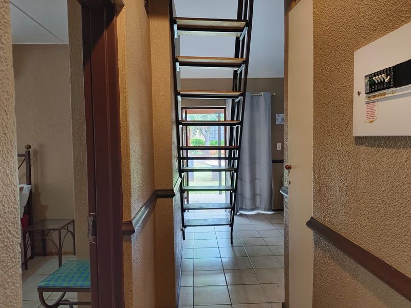 A hallway featuring a metal staircase leading to an upper level, tiled flooring, and a wall-mounted electrical distribution board.