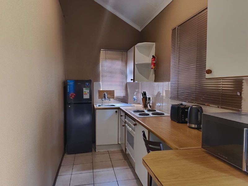 A compact, functional kitchen featuring laminate countertops, built-in cabinetry, an electric hob, oven, and tiled flooring with a neutral color palette.