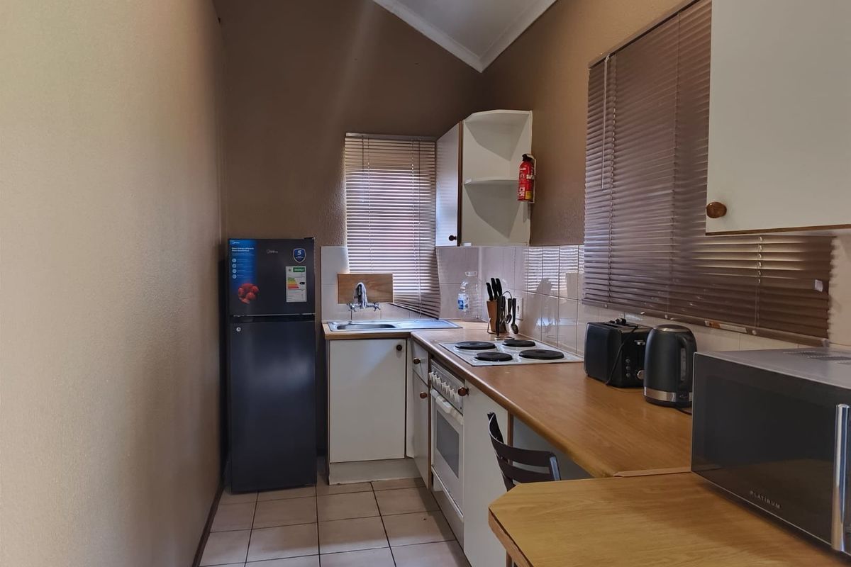 A compact, functional kitchen featuring laminate countertops, built-in cabinetry, an electric hob, oven, and tiled flooring with a neutral color palette.