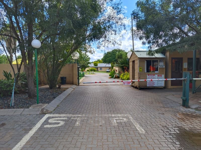 Entrance to the property featuring a paved driveway, security boom gate, and a dedicated guard booth.