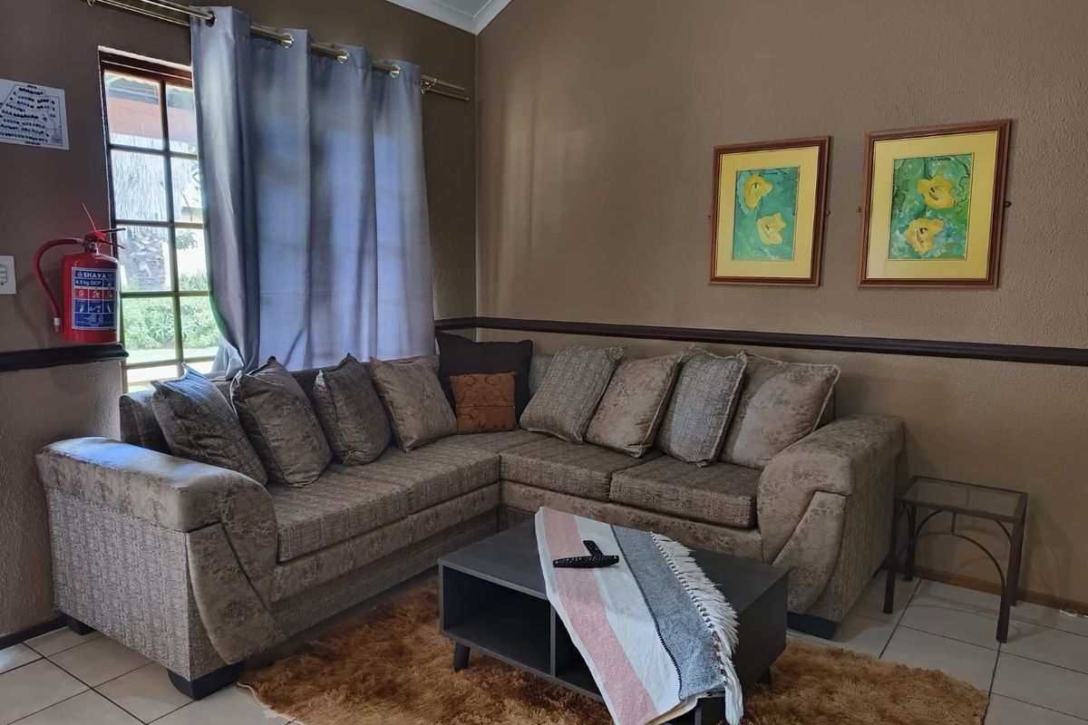A comfortable living room featuring tiled flooring, a vaulted ceiling, and a window with security bars, providing a functional and cozy space.