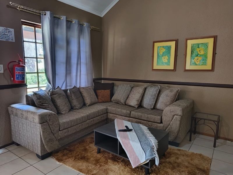 A comfortable living room featuring tiled flooring, a vaulted ceiling, and a window with security bars, providing a functional and cozy space.