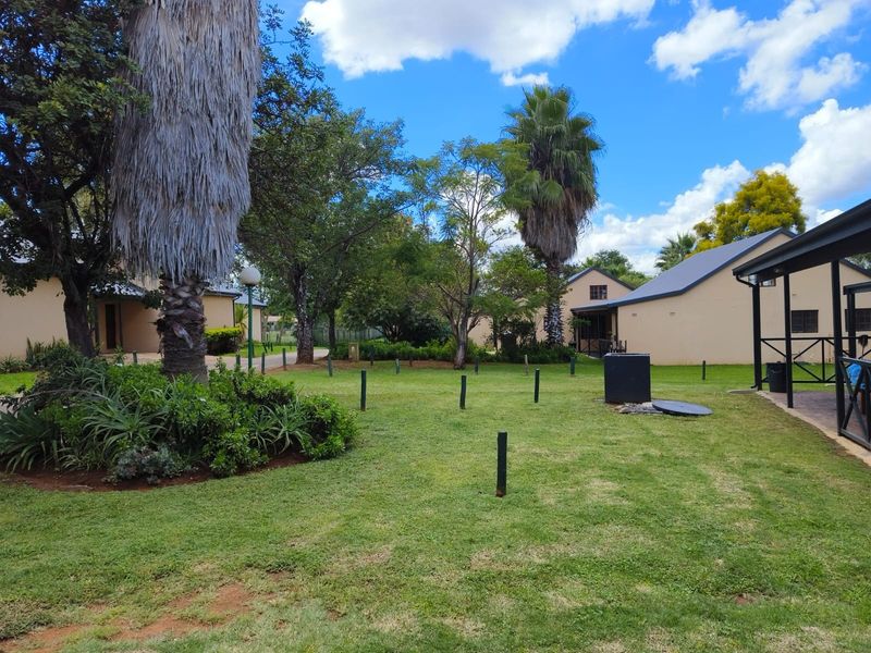 A well-maintained garden area featuring mature trees, a lush lawn, and a paved patio space adjacent to the residential building.