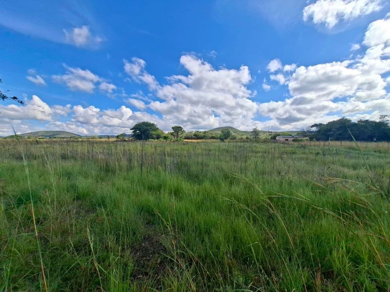 A wide-angle view of an undeveloped residential plot featuring natural grass and open landscape under a clear blue sky.