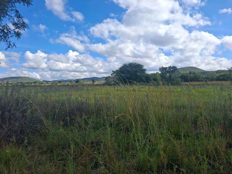 A scenic view of the vacant residential land featuring natural grassland and a mountainous horizon under a clear blue sky.