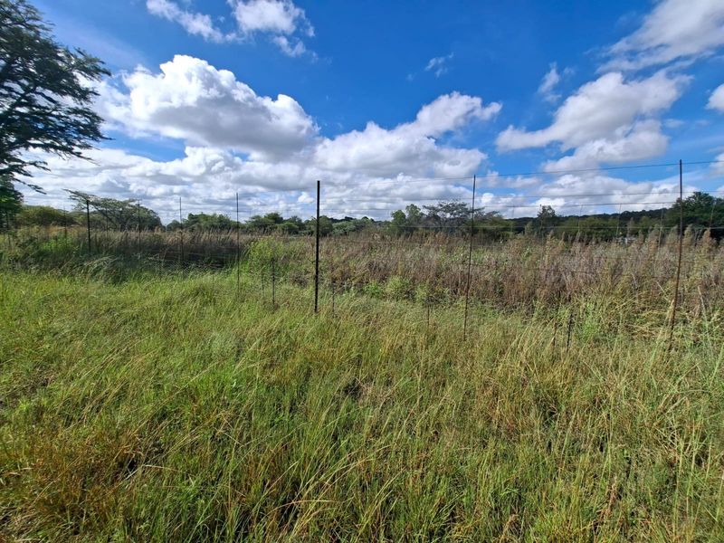 A view of a vacant residential plot featuring natural grass coverage and perimeter wire mesh fencing.