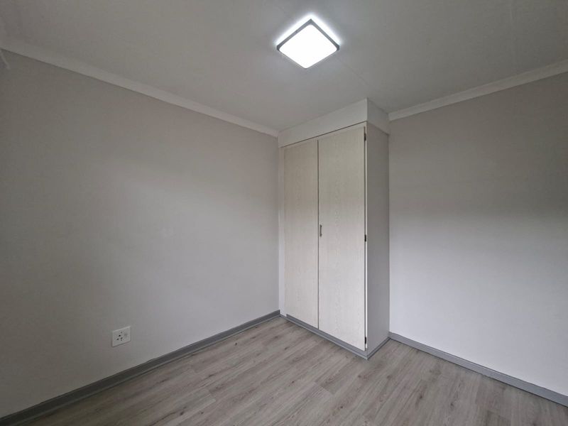 A clean, empty bedroom featuring modern laminate flooring, neutral walls, and a built-in wardrobe with light wood-grain finish.