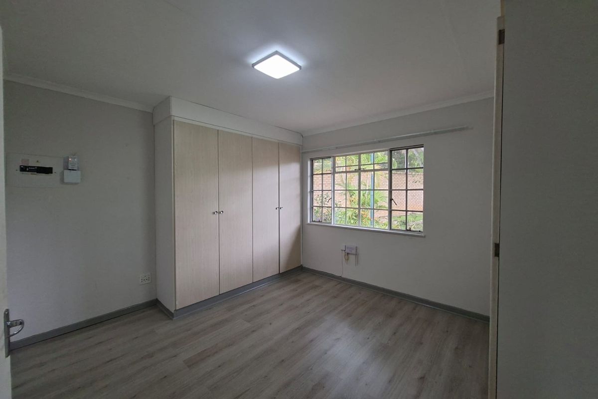 A clean, empty bedroom featuring light-toned laminate flooring, built-in cupboards, and a window providing natural light.
