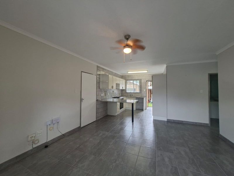 An open-plan living and kitchen area featuring tiled flooring, a ceiling fan, and a functional kitchen with built-in cabinetry and granite countertops.
