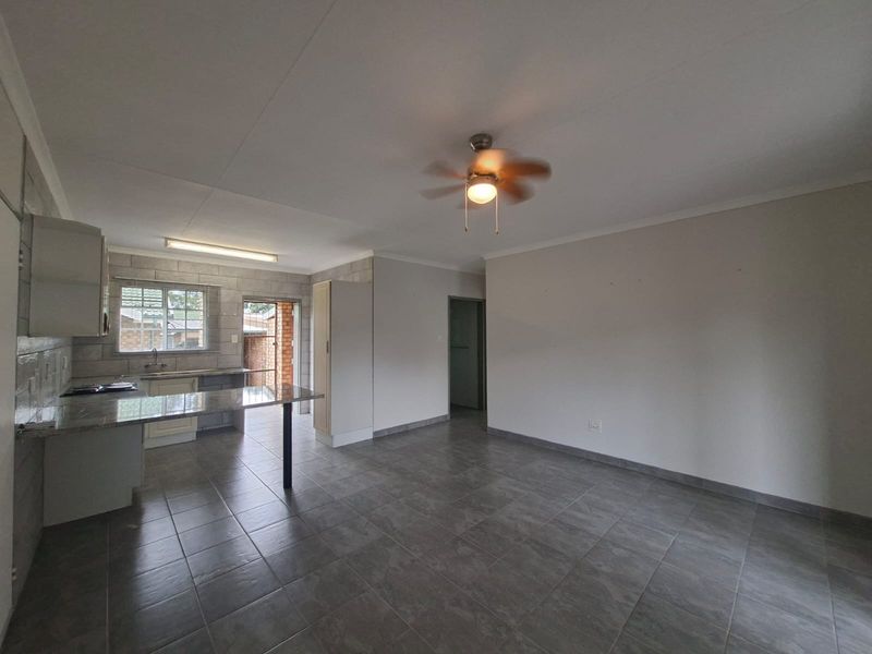 Spacious open-plan living area featuring tiled floors, a ceiling fan, and a functional kitchen with granite countertops and built-in cabinetry.