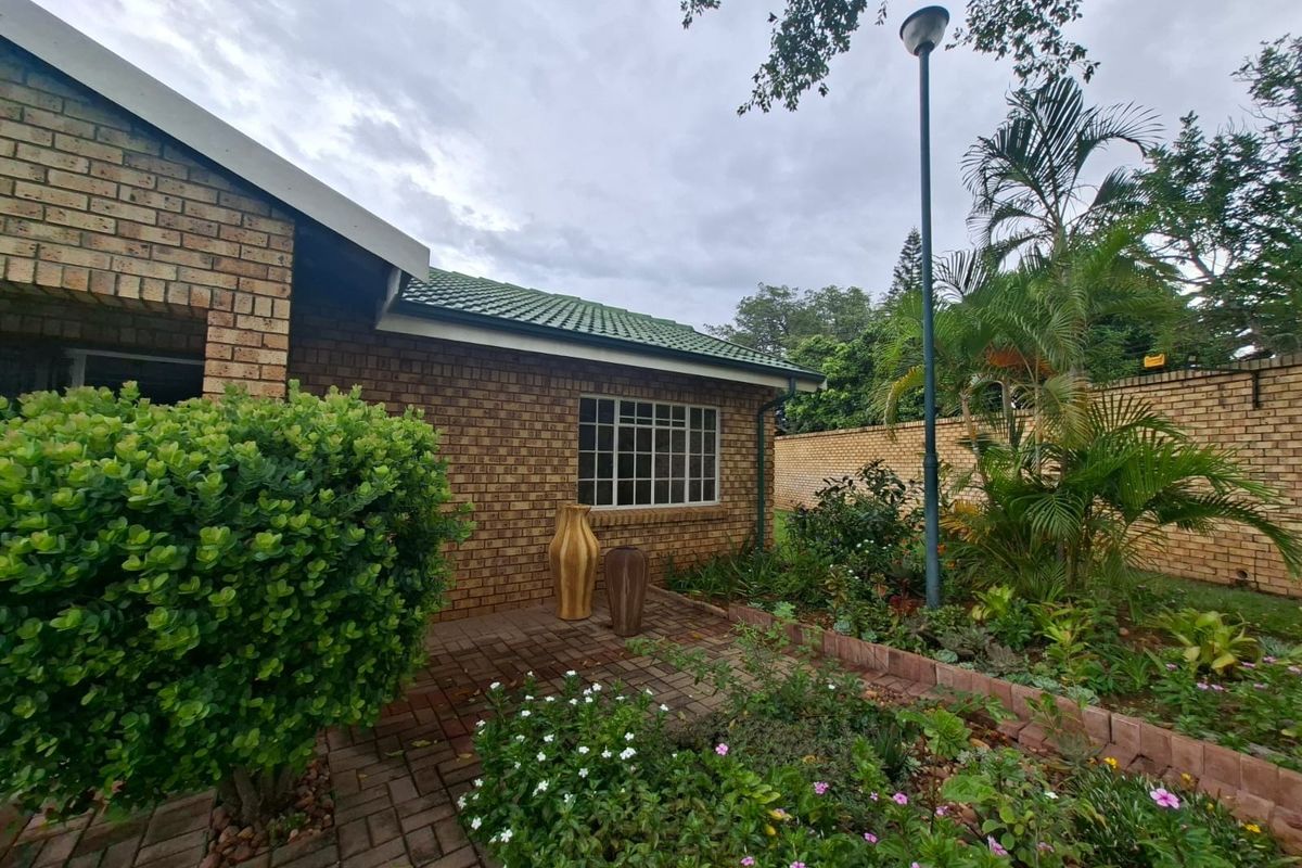 A well-maintained rear exterior view featuring a face brick facade, paved patio area, and established garden with perimeter walling.