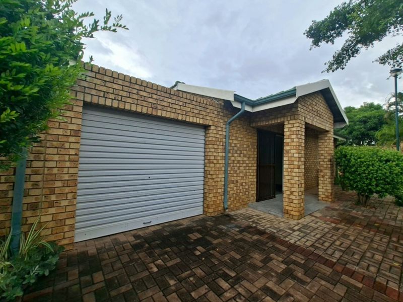 Front exterior view of a face brick retirement unit featuring a roller shutter garage door, covered entrance, and paved driveway area.