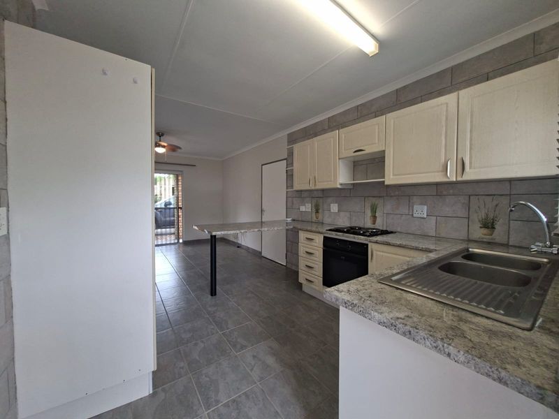 Open-plan kitchen featuring granite countertops, built-in oven and hob, tiled backsplash, and a breakfast bar, flowing into an adjacent living area.