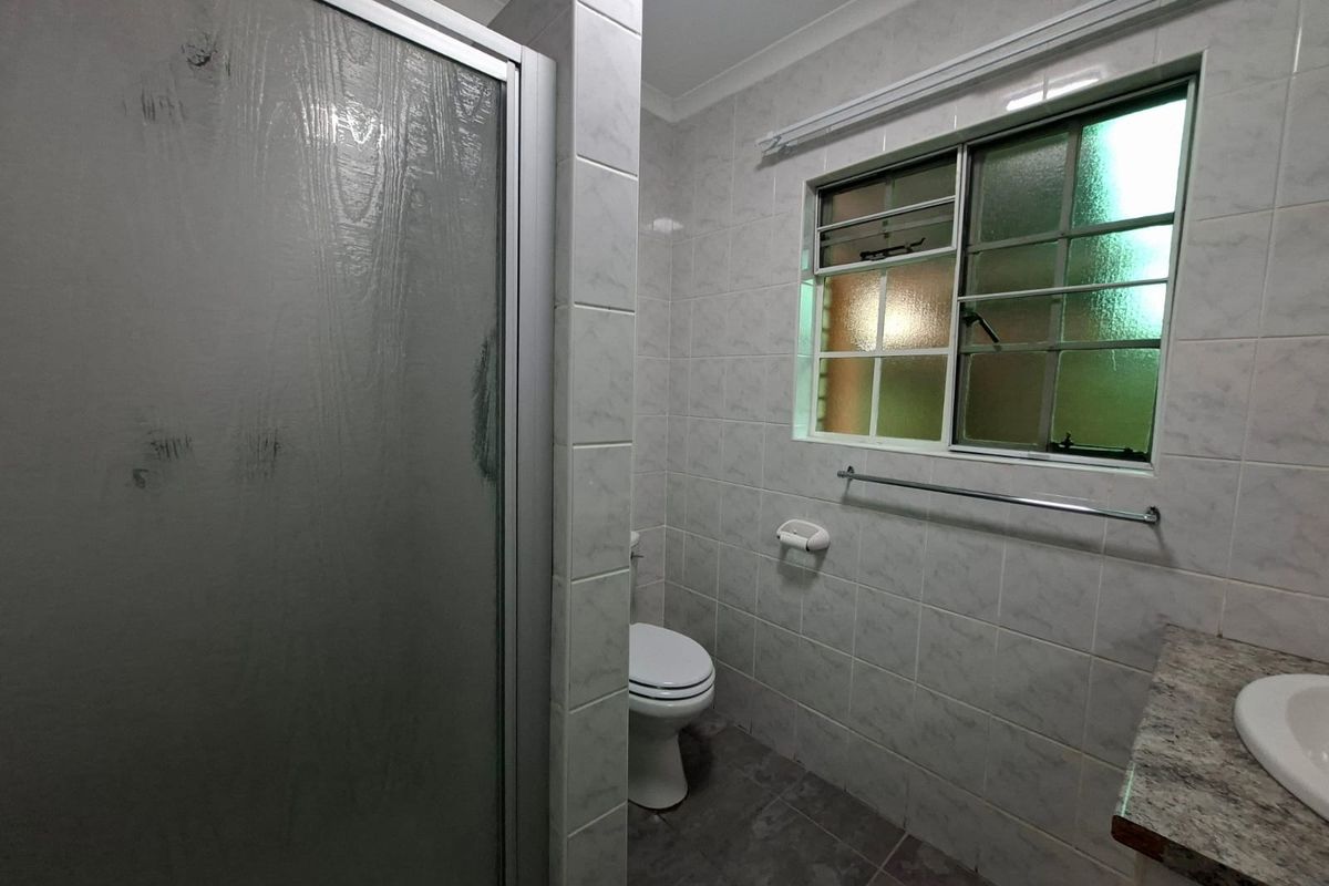 A functional bathroom featuring a shower enclosure, toilet, and vanity basin with tiled finishes and a louvered window for ventilation.