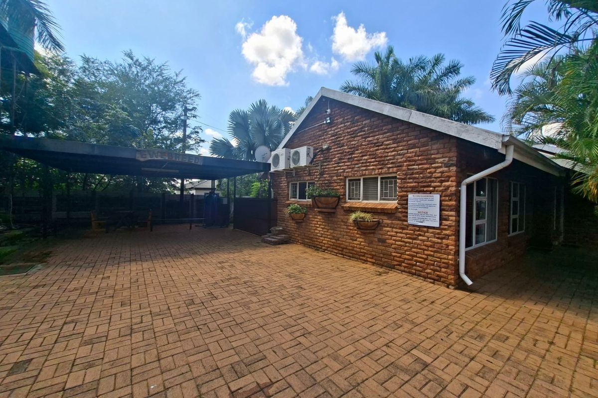 Rear exterior view of the guest house featuring a paved courtyard, covered patio area, and exposed brick facade with mounted air conditioning units.