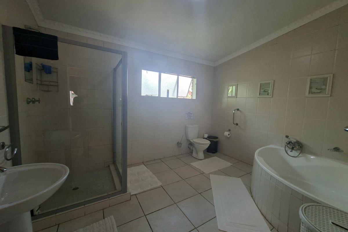 Spacious bathroom featuring a separate shower enclosure, built-in bathtub, pedestal basin, and toilet with neutral wall and floor tiling.