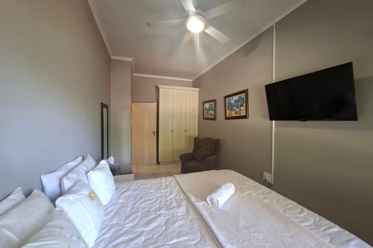 A well-maintained bedroom featuring neutral wall tones, tiled flooring, a ceiling fan, and built-in wardrobe storage.