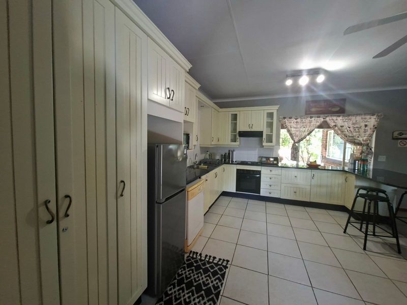 A functional kitchen featuring cream-colored cabinetry, granite countertops, built-in oven, extractor fan, and tiled flooring with a breakfast bar area.