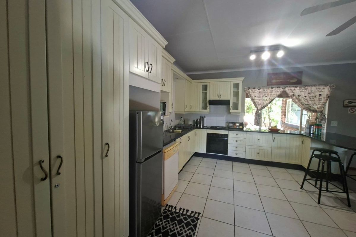 A functional kitchen featuring cream-colored cabinetry, granite countertops, built-in oven, extractor fan, and tiled flooring with a breakfast bar area.