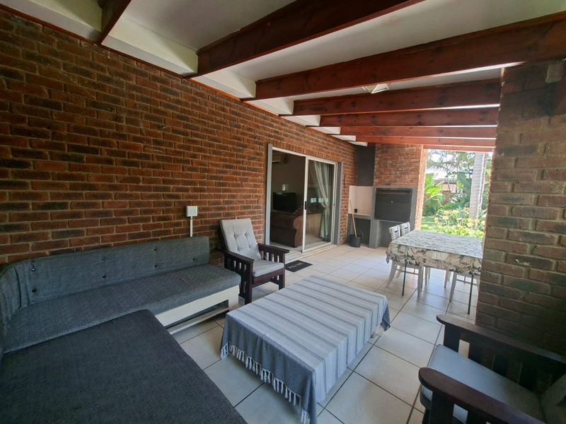 A covered patio area featuring exposed timber beams, brick walling, and a built-in braai, providing a functional outdoor entertainment space.