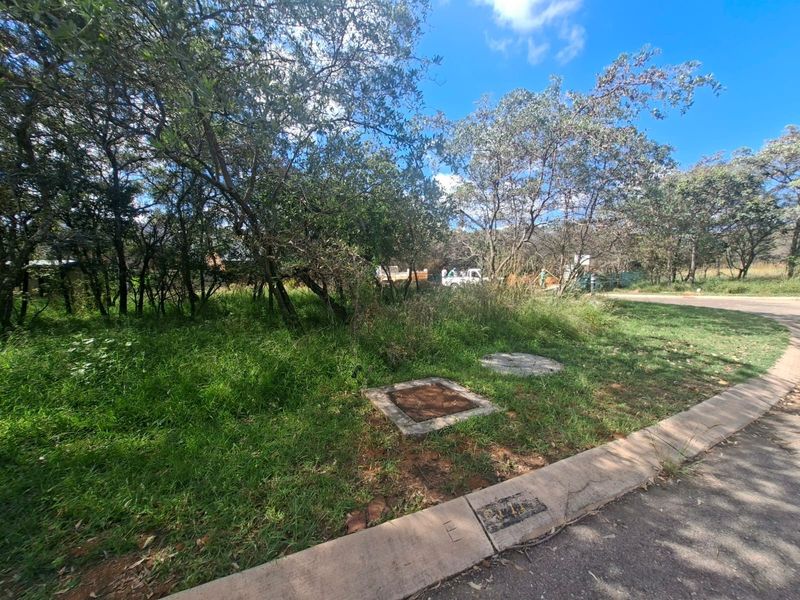 A view of the street frontage and access point for the vacant residential land, featuring established trees and existing utility access points.
