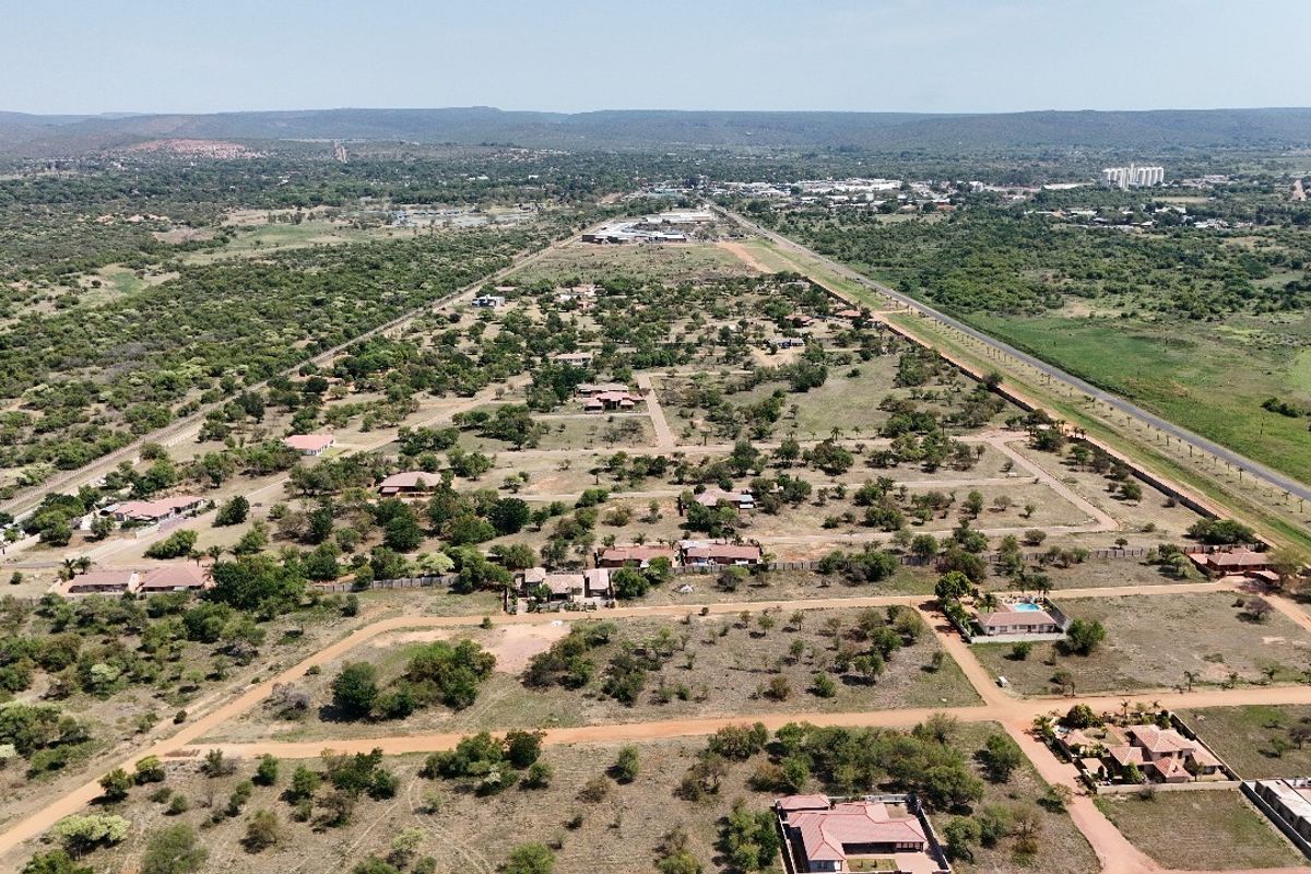 An aerial view of a residential development area featuring multiple plots, dirt roads, and surrounding natural landscape.
