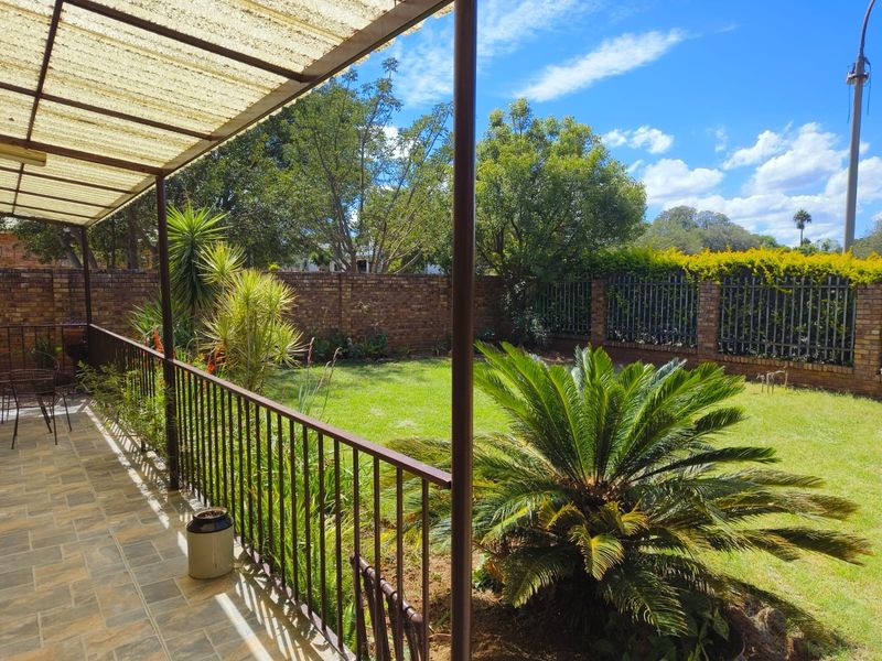 A covered patio area overlooking a private garden with established landscaping, brick boundary walls, and metal security fencing.
