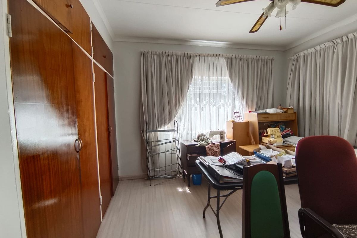 A bedroom featuring built-in wooden cupboards, laminate flooring, and a ceiling fan, offering a functional space with potential for modernization.