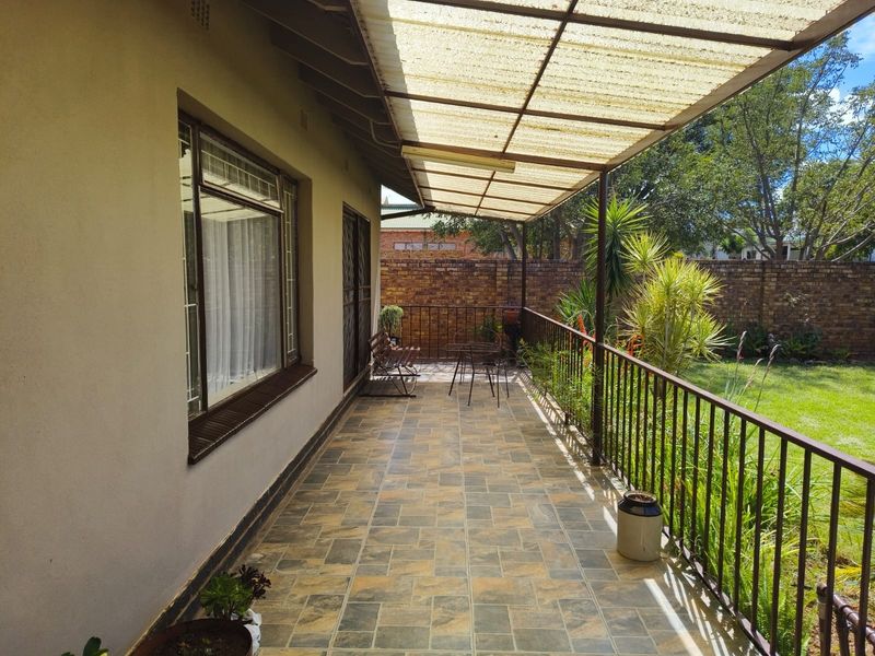 A covered patio area featuring tiled flooring, a metal balustrade, and a translucent roof, overlooking a private garden with a brick boundary wall.