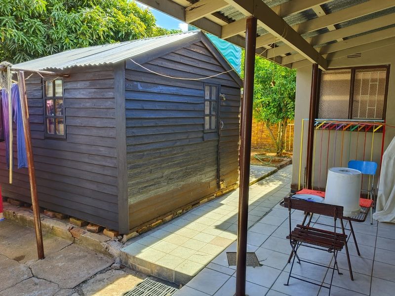 A rear outdoor area featuring a timber garden shed, a tiled patio, and a covered veranda structure with steel support posts.