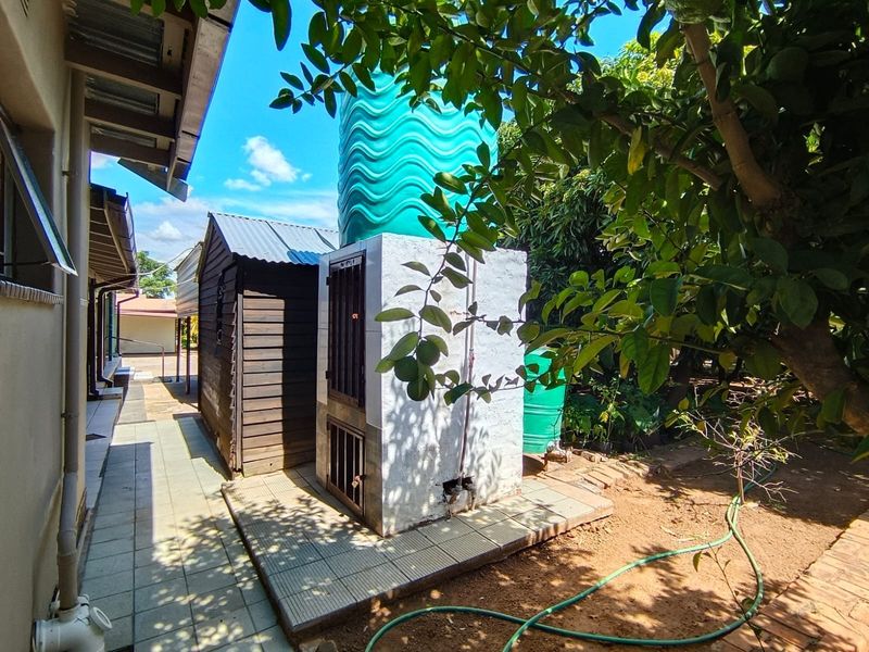 Rear exterior area featuring a water storage tank on a masonry plinth, adjacent to a timber shed and paved walkway.