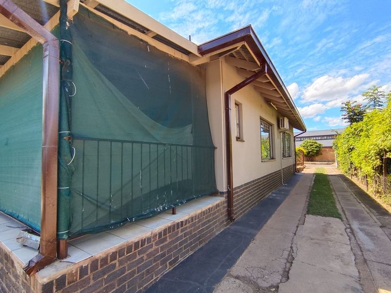 Rear exterior view of the house featuring a tiled patio area, brick facade, and a concrete pathway leading along the side of the property.