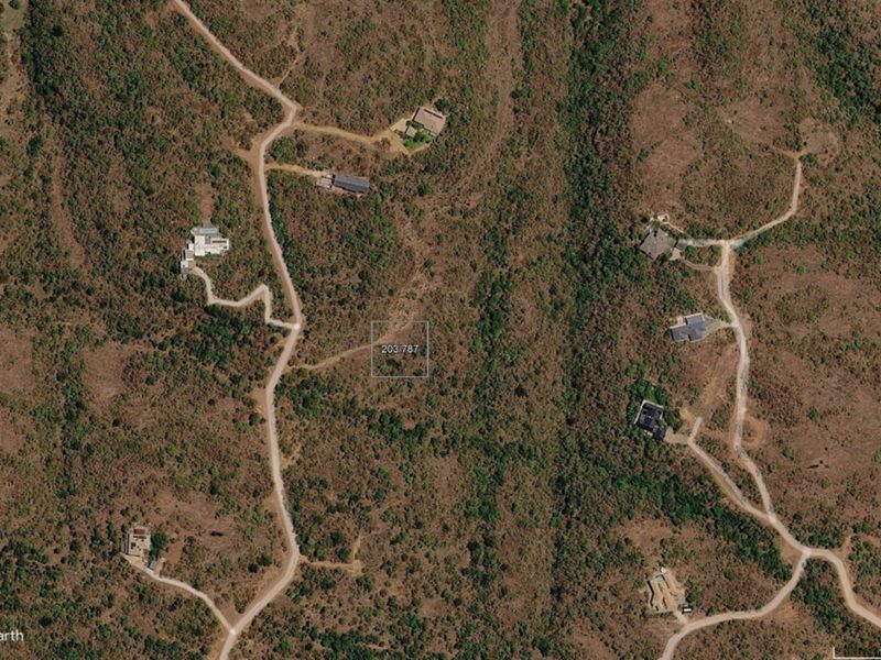 Aerial view of a vacant residential plot situated within a natural landscape, featuring surrounding access roads and nearby established properties.
