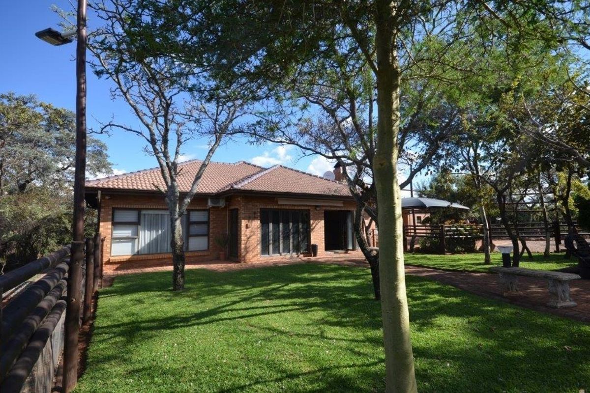 Rear view of a brick house featuring a tiled roof, paved patio area, and a well-maintained garden with mature trees.