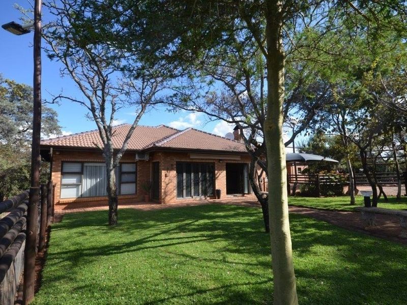 Rear view of a brick house featuring a tiled roof, paved patio area, and a well-maintained garden with mature trees.