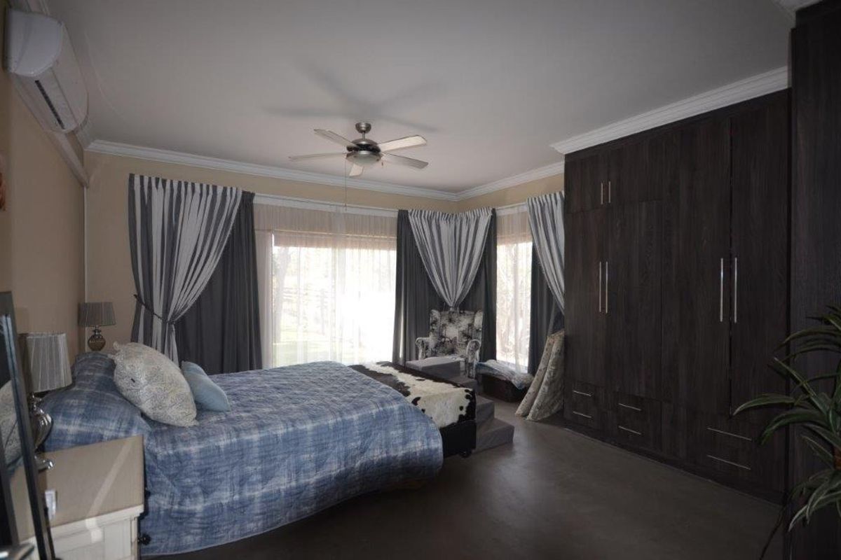 Spacious bedroom featuring dark wood built-in cupboards, a ceiling fan, and a wall-mounted split-system air conditioner.