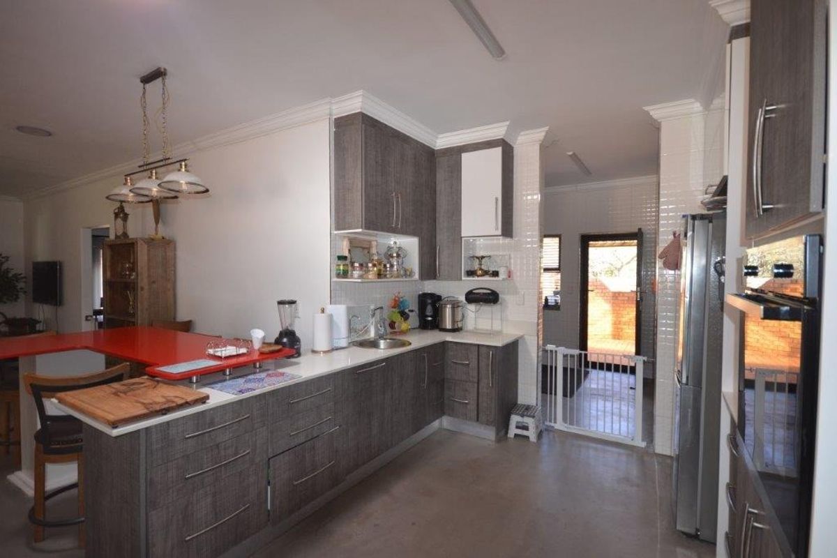 Modern kitchen featuring dark wood-grain cabinetry, stone countertops, integrated oven, and a tiled splashback, with an open-plan layout leading to a rear exit.