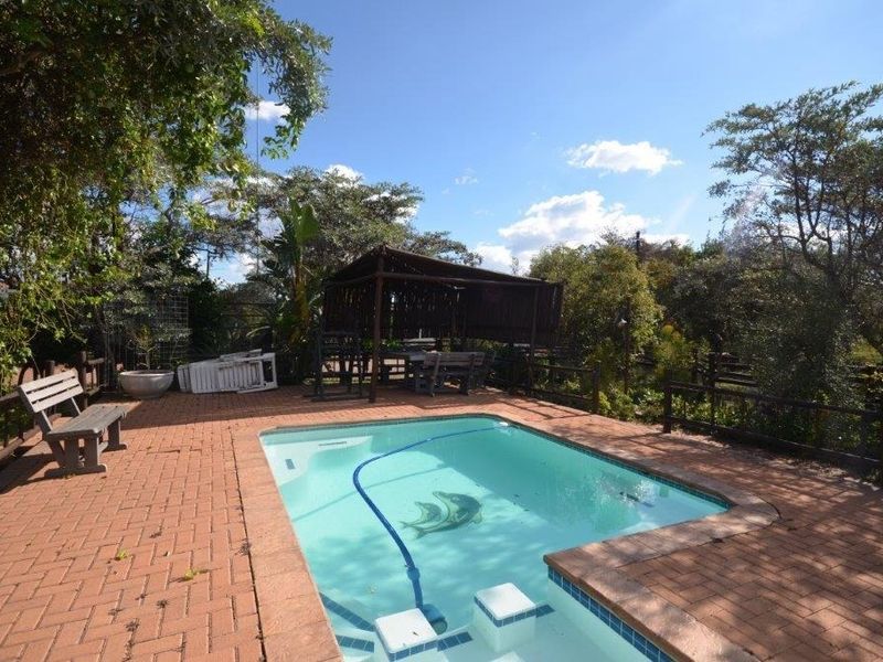 Outdoor pool area featuring a swimming pool, brick paved surround, and a timber gazebo set within a garden environment.