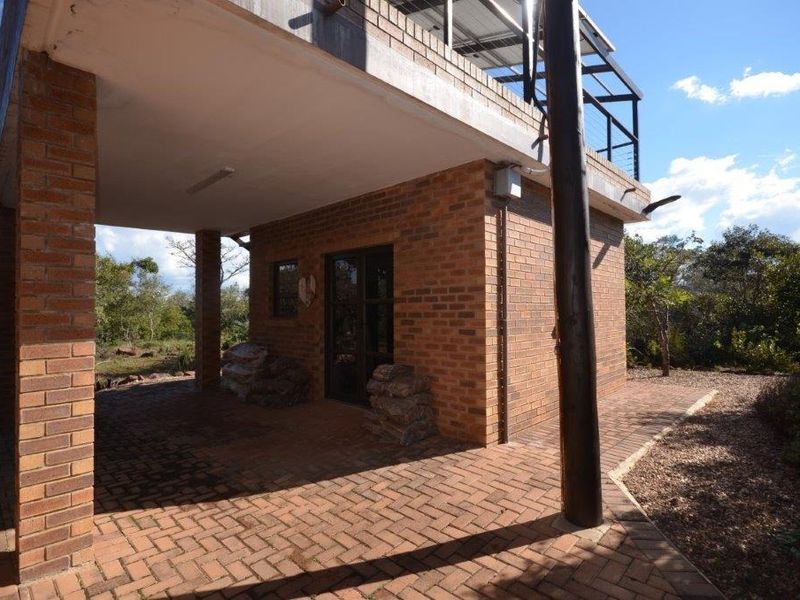 A covered brick patio area featuring exposed brickwork and a timber support column, providing a sheltered outdoor space with an adjacent balcony above.