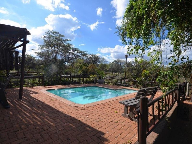 Outdoor pool area featuring brick paving, a timber pergola, and wooden fencing, set within a natural garden environment.