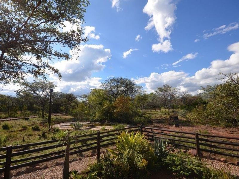 A spacious outdoor garden area featuring timber post and rail fencing, established landscaping, and natural bushveld surroundings.
