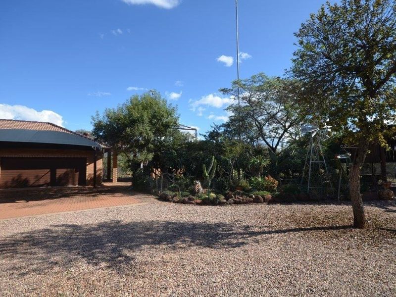 Front exterior view featuring a gravel driveway, brick paved area, double garage with shade sail, and a landscaped garden with a decorative windmill.