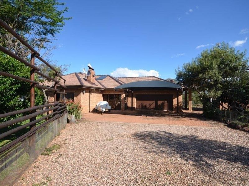 Front exterior view of a brick house featuring a paved driveway, carport, and established garden surroundings.