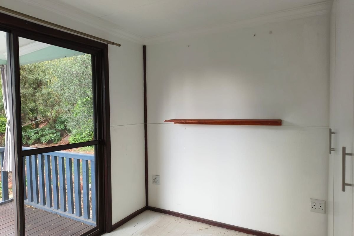 An empty bedroom featuring a sliding glass door with access to a deck, built-in cupboards, and a wall-mounted wooden shelf.