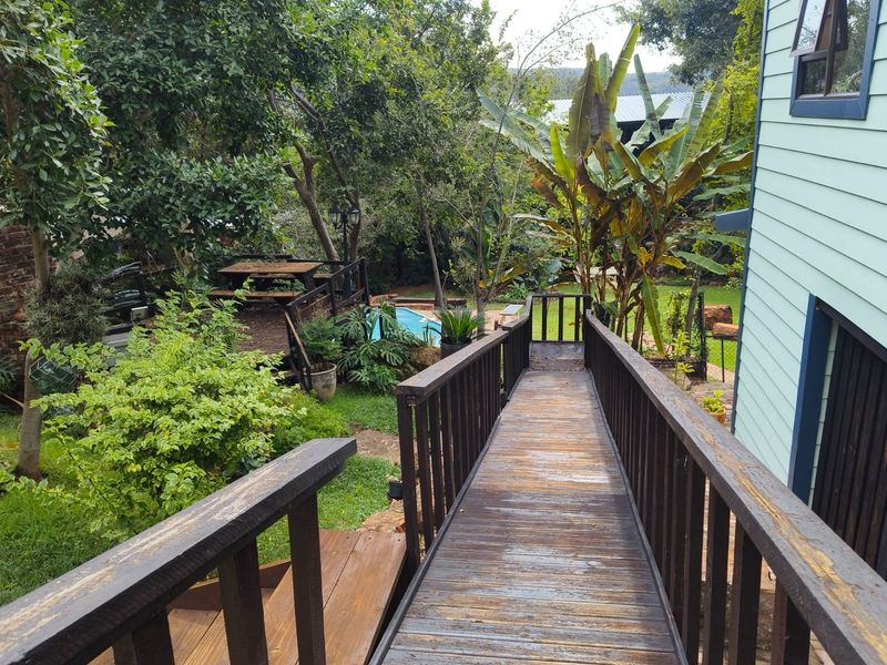 Rear view featuring a wooden walkway leading to a garden area with a swimming pool and timber decking, set against a lush backyard.