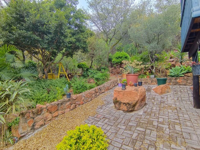 A landscaped garden area featuring a stone retaining wall, paved patio space, and natural rock features set within a lush, mature garden setting.