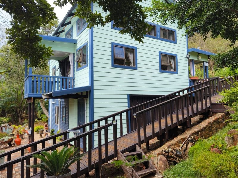 A multi-level timber-clad house featuring a raised wooden ramp and deck, set against a natural garden with stone retaining walls.