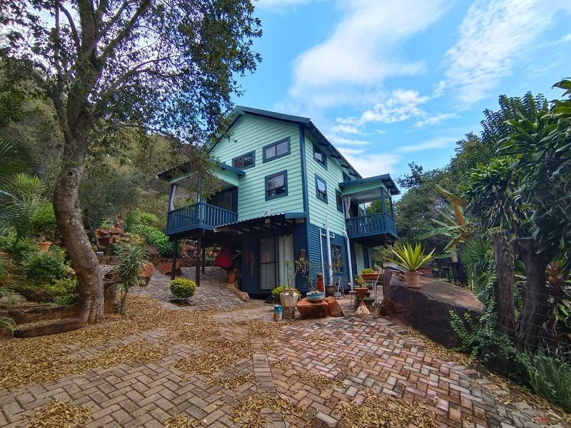 A multi-level timber-clad house featuring raised balconies, set within a landscaped garden with paved pathways and natural rock features.