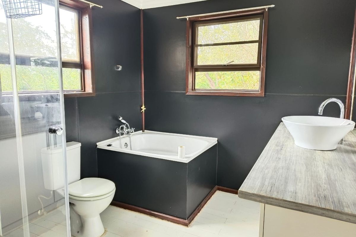 Bathroom featuring a built-in bathtub, glass shower enclosure, vessel sink on a vanity countertop, and dark wall finishes.